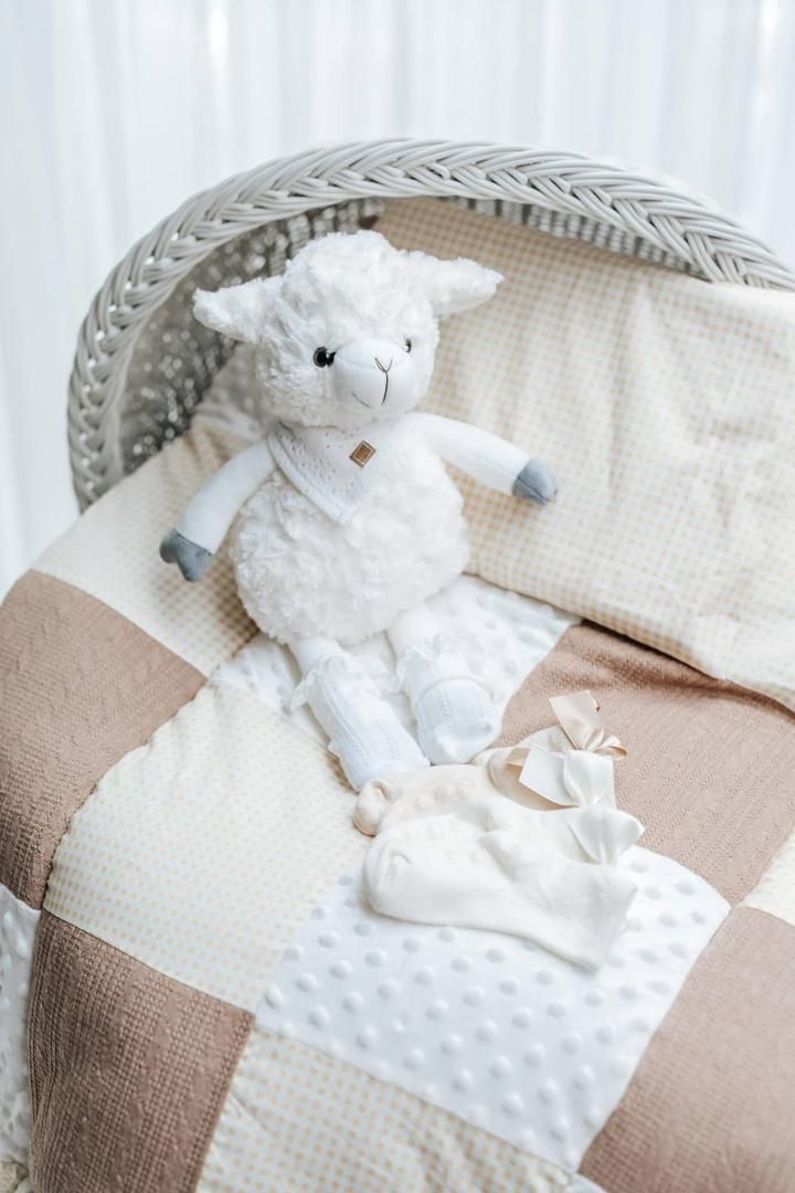 White plush lamb toy sitting on a checkered blanket with baby accessories.