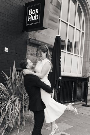 A couple shares a romantic dance pose together against a brick building exterior.