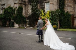 Bride and groom holding hands outside a Scottish castle venue, groom wearing traditional tartan kilt.