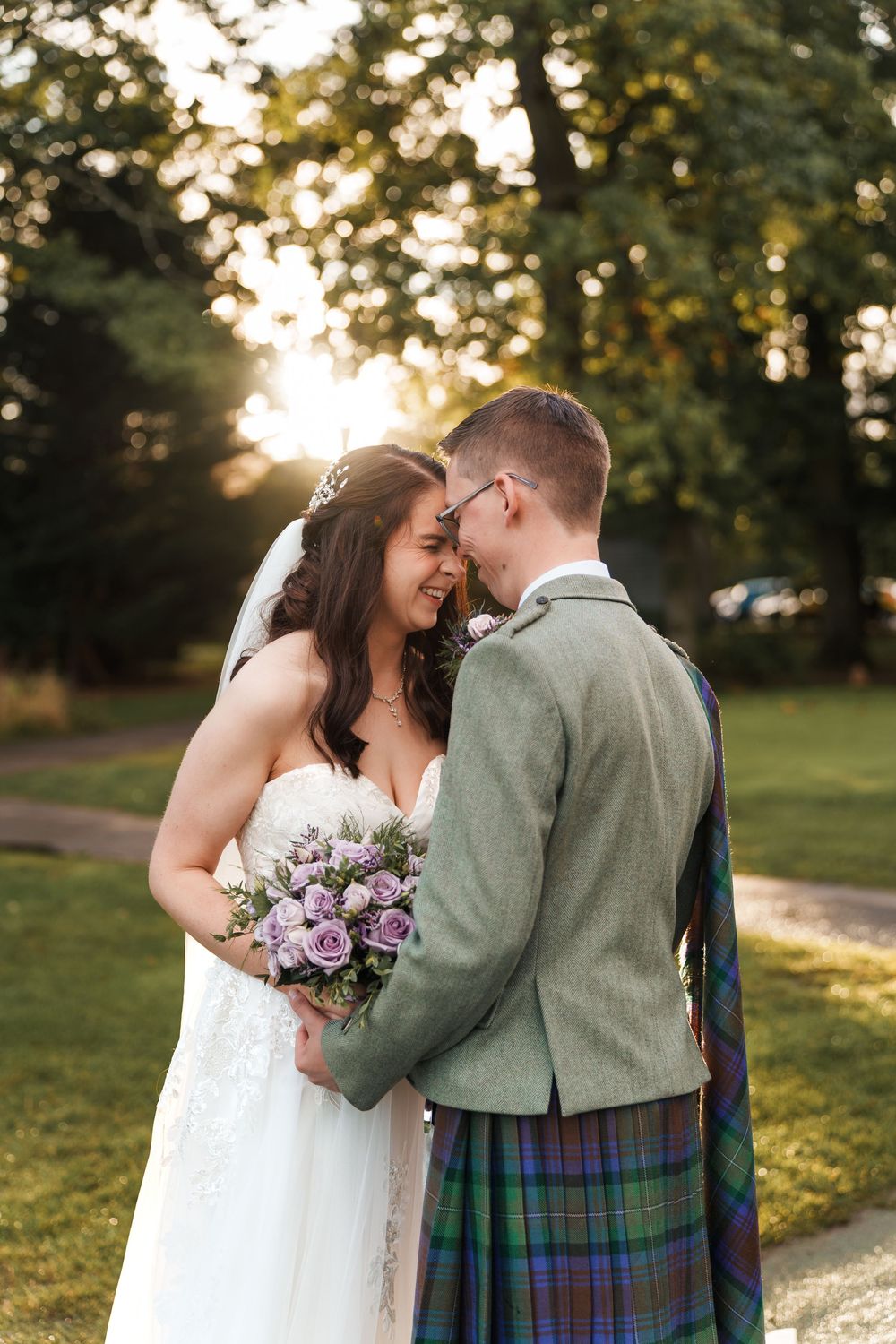 A romantic wedding photo shoot in a park at sunset with the groom wearing traditional Scottish highland dress.