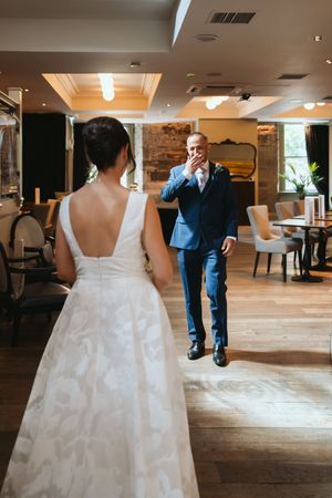 Wedding party members in formal attire dance and socialize on an elegant hardwood floor at an indoor reception venue.