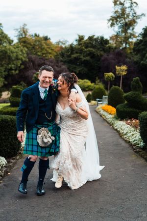 A sweet moment between a couple in wedding attire kneeling on a garden path surrounded by flowers.
