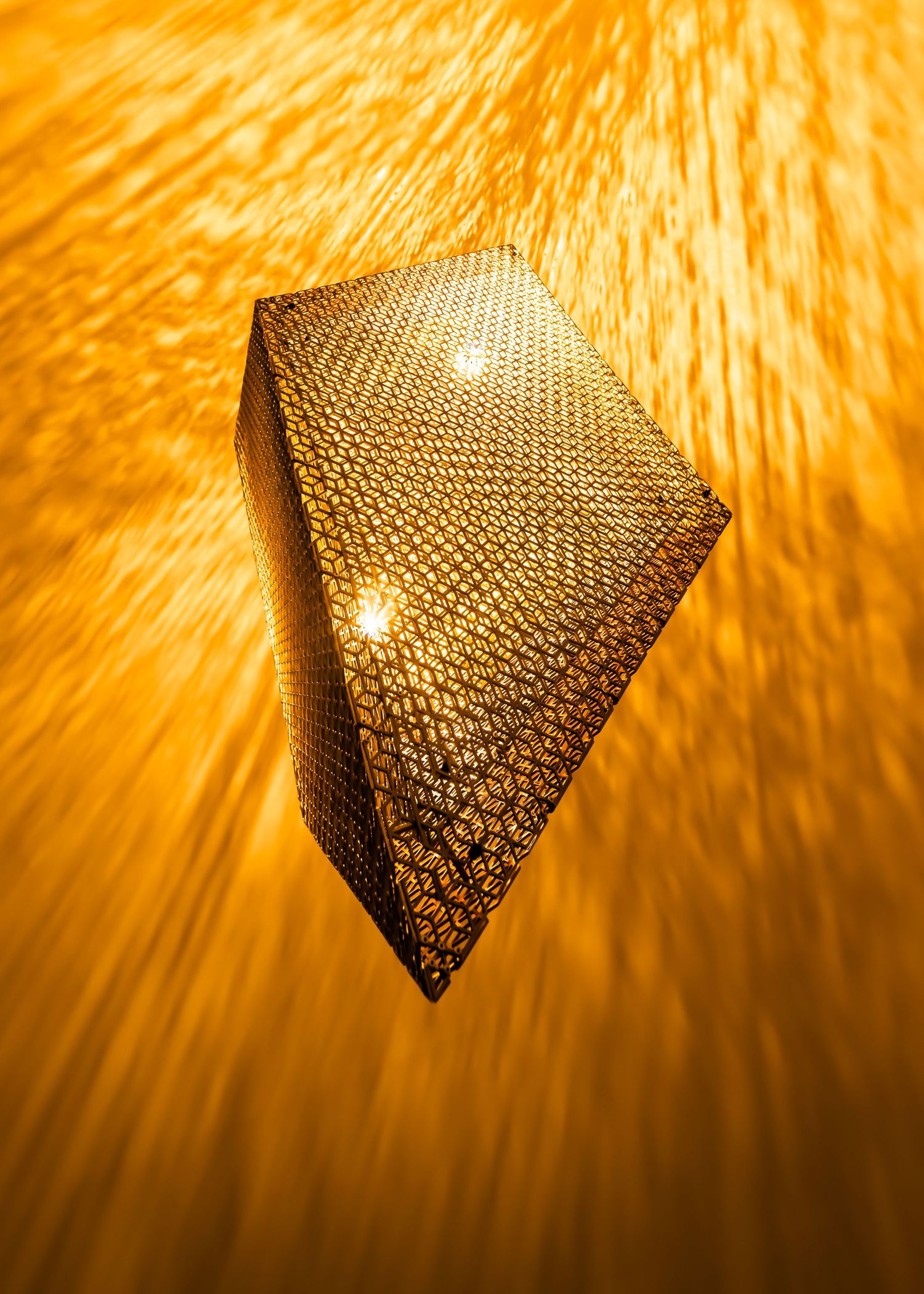 A golden geometric wall sconce casting dramatic shadows and light patterns against an orange-tinted background.