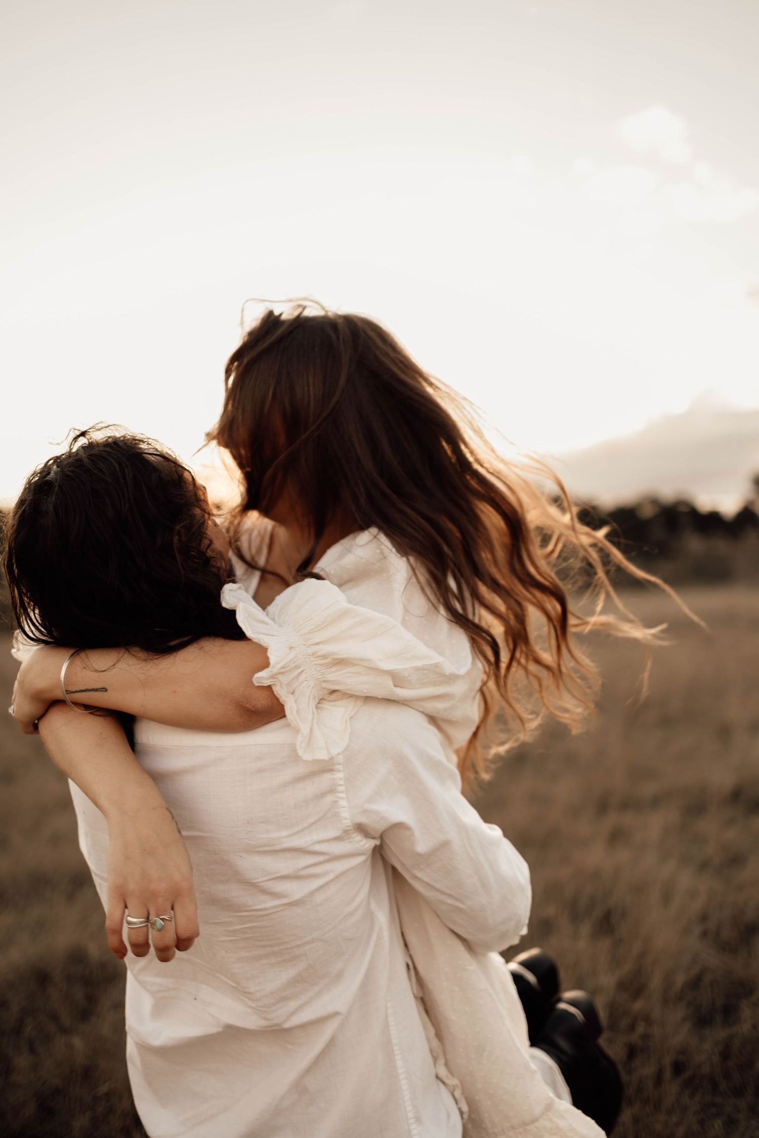 Couple in vintage-inspired outfits holding hands while walking through a golden sunlit field at sunset.