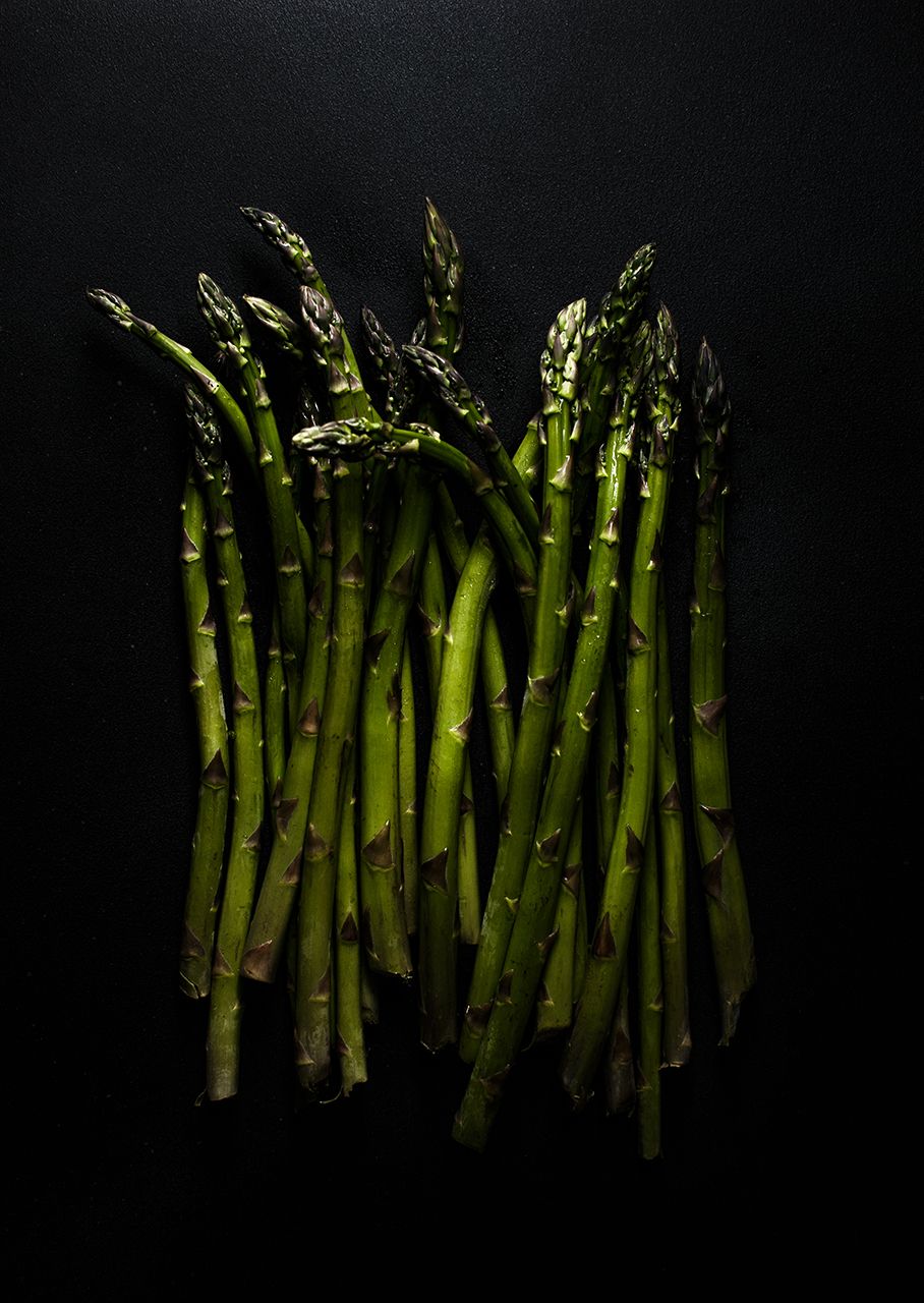 Fresh green asparagus spears arranged in a row on black background. Producing high-quality visuals for product advertisements