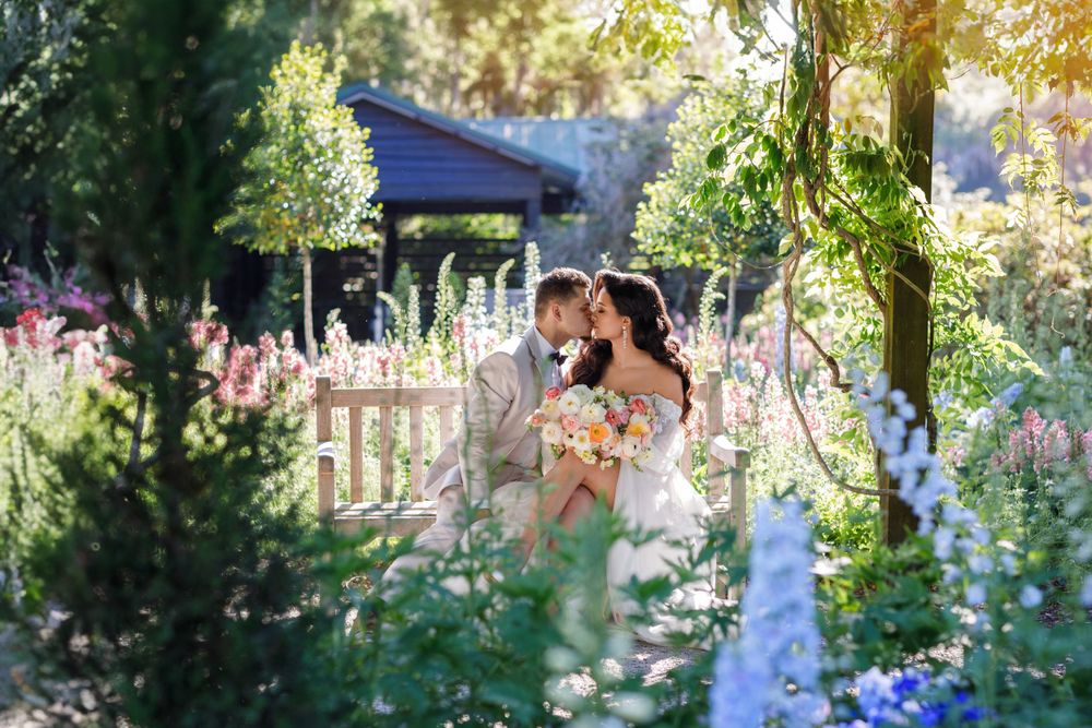 A tender moment captured in a garden filled with blooming delphiniums and summer flowers.