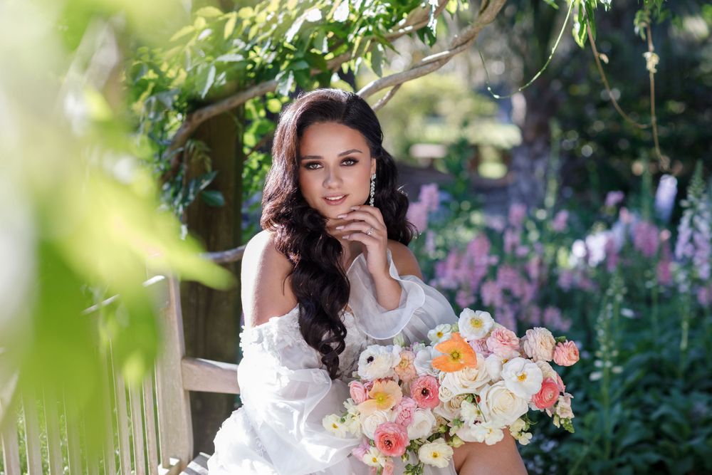 A bridal portrait in a garden setting with purple flowers and a peach and white bouquet.