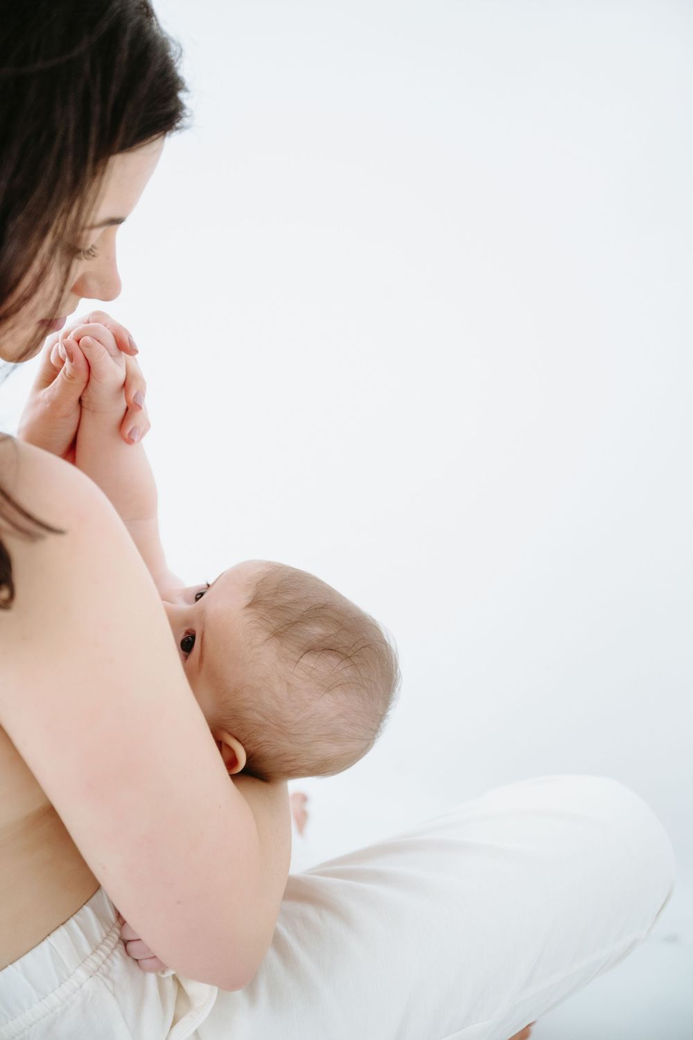 A mother tenderly breastfeeding her newborn baby against a soft white background.