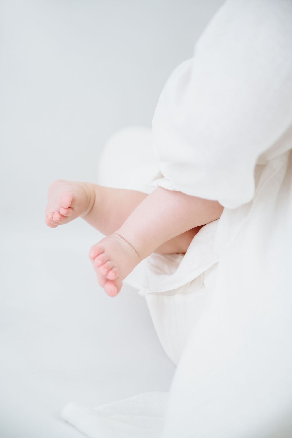 Close-up of tiny newborn baby feet wrapped in soft white fabric against a white background.