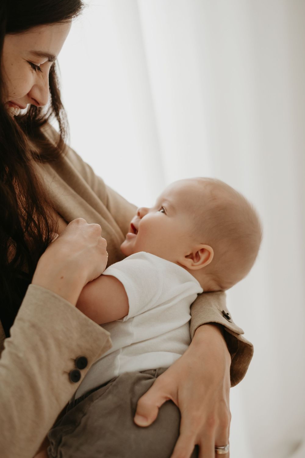 A smiling mother tenderly holds her happy baby in her arms, sharing a loving moment together.