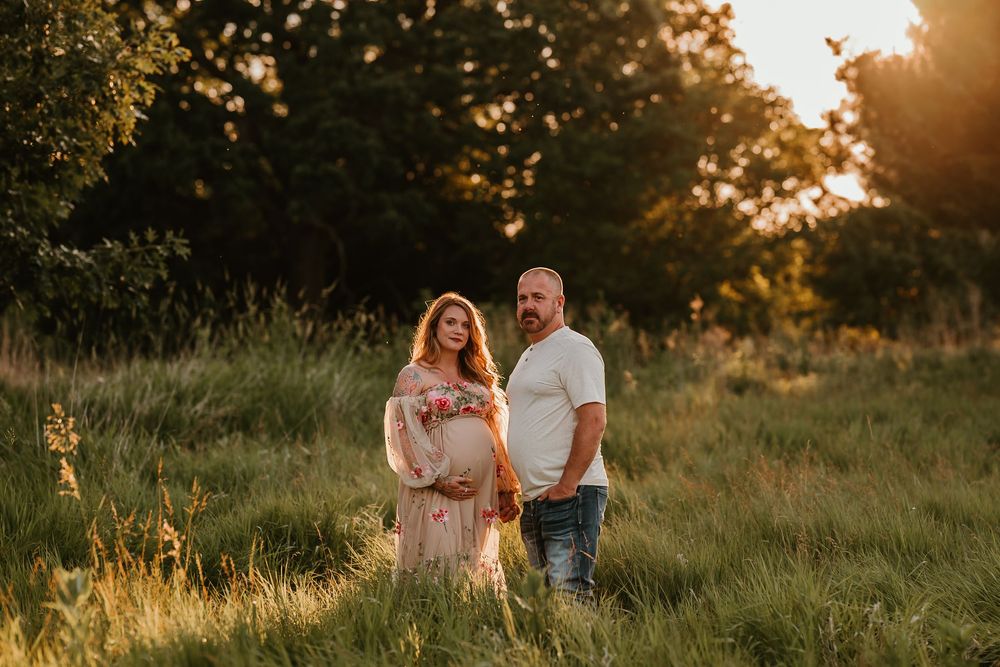 Dreamy outdoor photo session in a field at golden hour with soft sunlight filtering through trees.