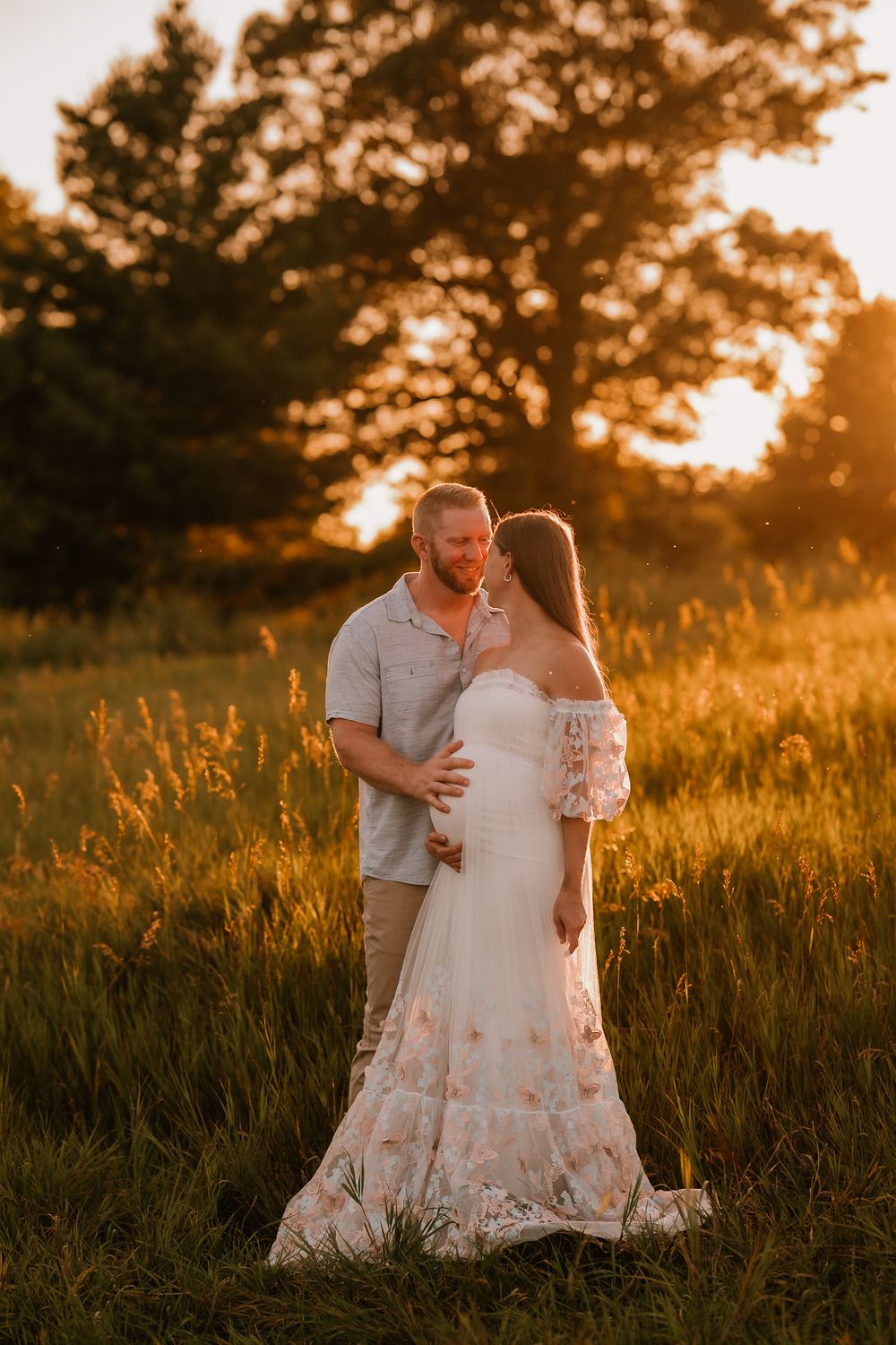 A romantic sunset maternity photoshoot in a golden wildflower field features a couple embracing in beautiful lighting.