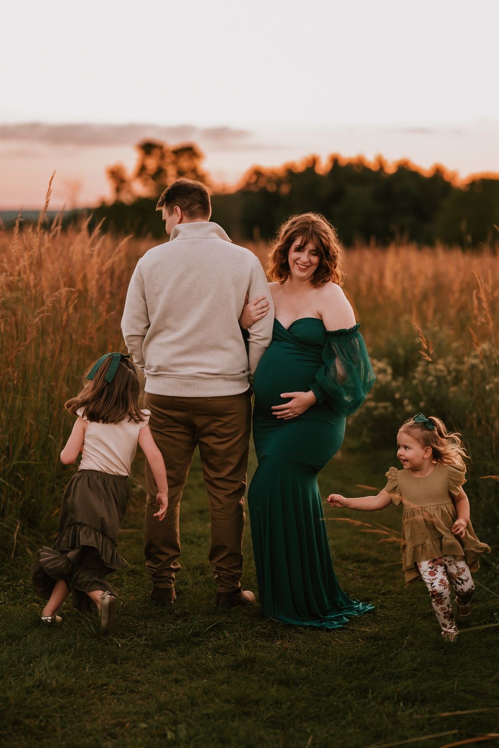 A family of four enjoying a sunset moment together in a field of tall grass during a maternity photo session.
