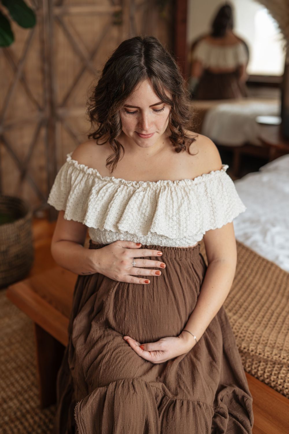 Woman in brown off-shoulder dress with white lace trim poses for maternity photos.