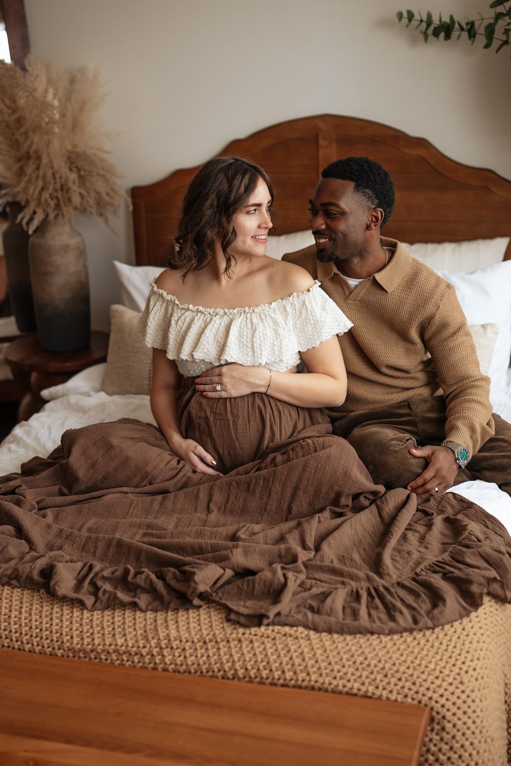 A couple shares an intimate moment while lying together on a brown bed with textured bedding and wooden headboard.