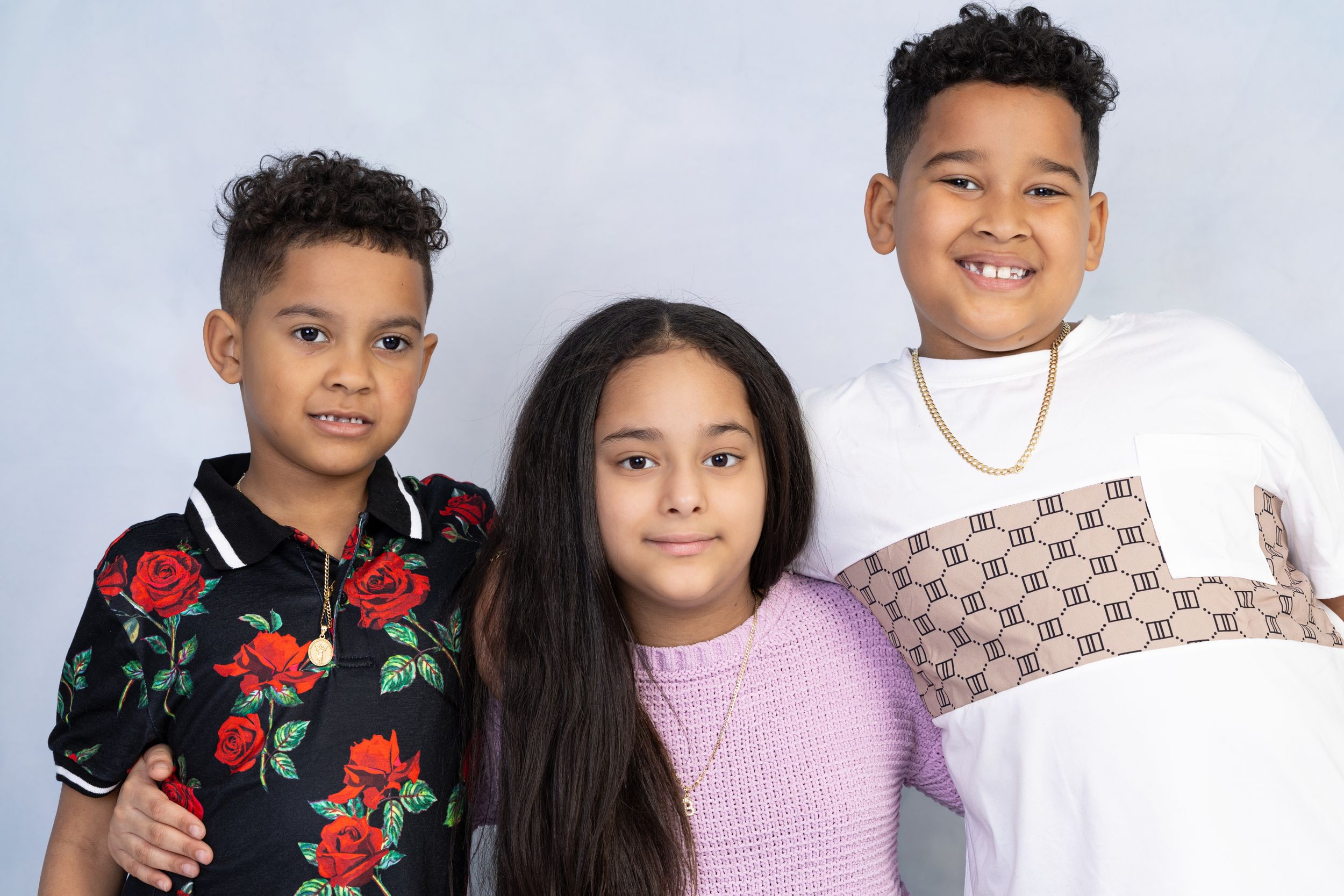 Three young people posing together in coordinated casual outfits against blue background.