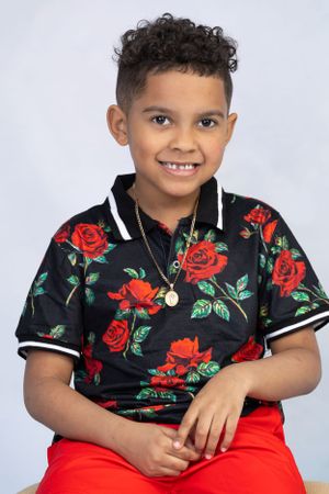 Young person in black floral polo shirt with red roses and red shorts against light background.