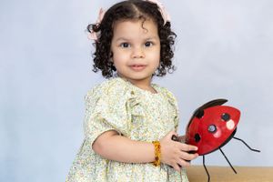 Small child in floral dress holding red ladybug toy against light blue background.
