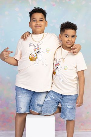 Two young brothers in matching graphic tees and denim shorts pose together against pastel background.