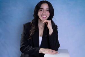 Professional business portrait against blue backdrop with classic black blazer.