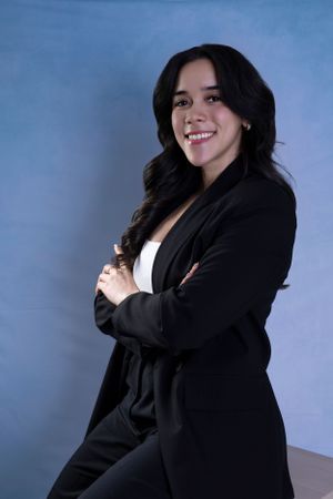 Professional studio portrait of a smiling woman in black blazer against blue background.