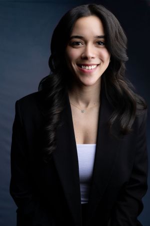 Close-up headshot of woman wearing black blazer and white top with dark wavy hair.