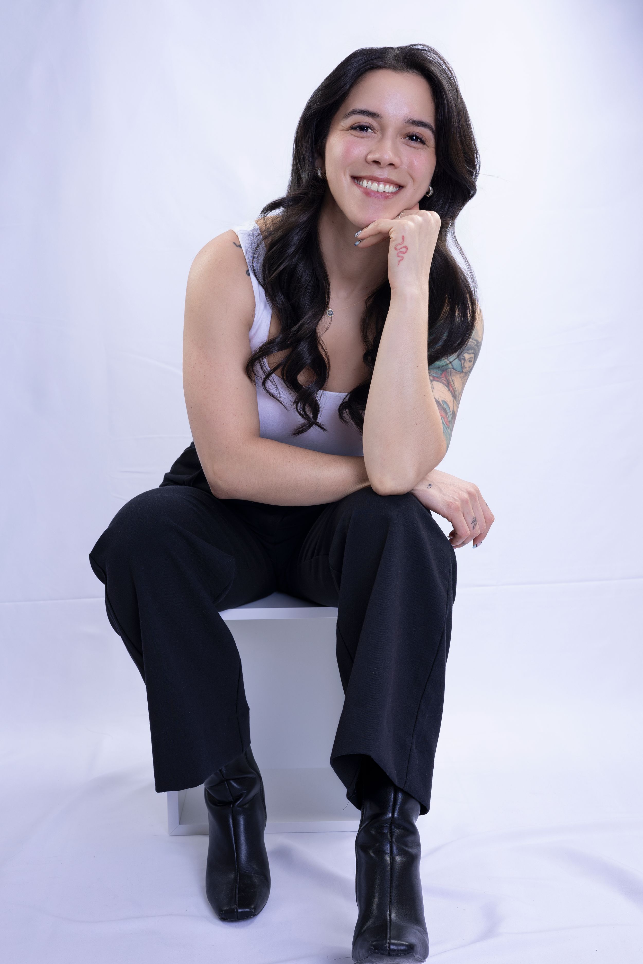 Casual studio portrait of person in gray tank top and black pants sitting on white background.