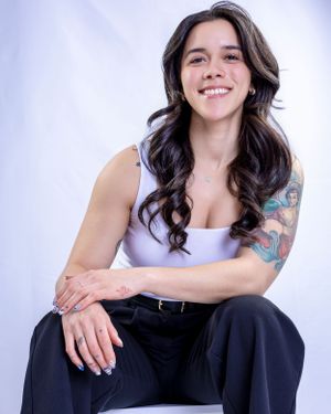 Relaxed seated portrait showing colorful arm tattoo and casual style.