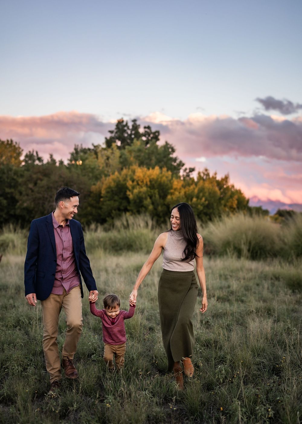 A couple walks hand in hand through a scenic field at sunset with trees in the background creating a romantic silhouette.