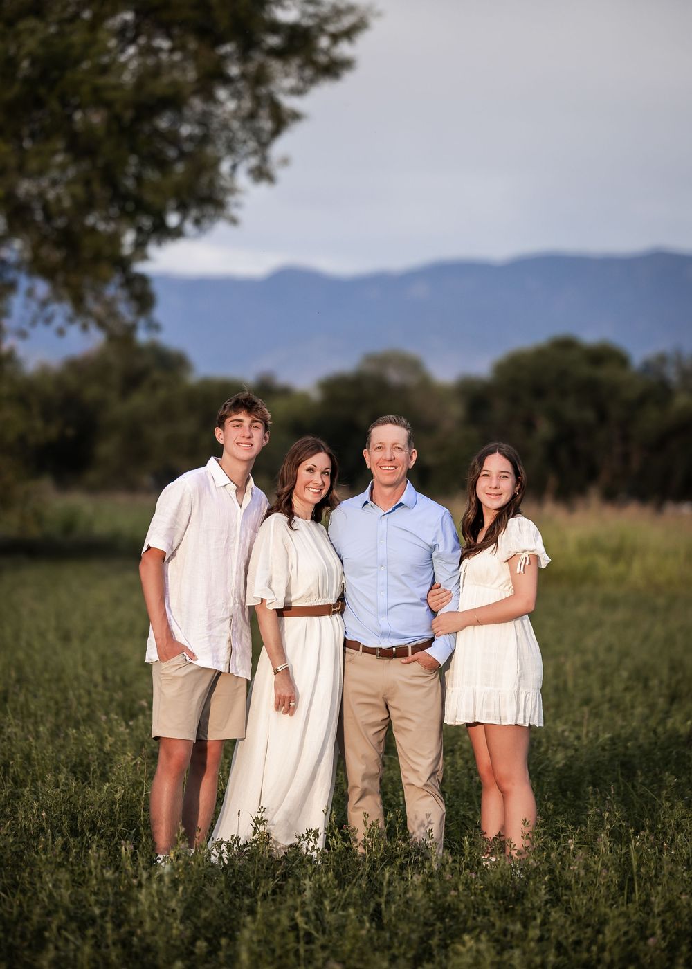 A multi-photo series shows a group in light-colored clothing posing together in a grassy field with mountains in the background.