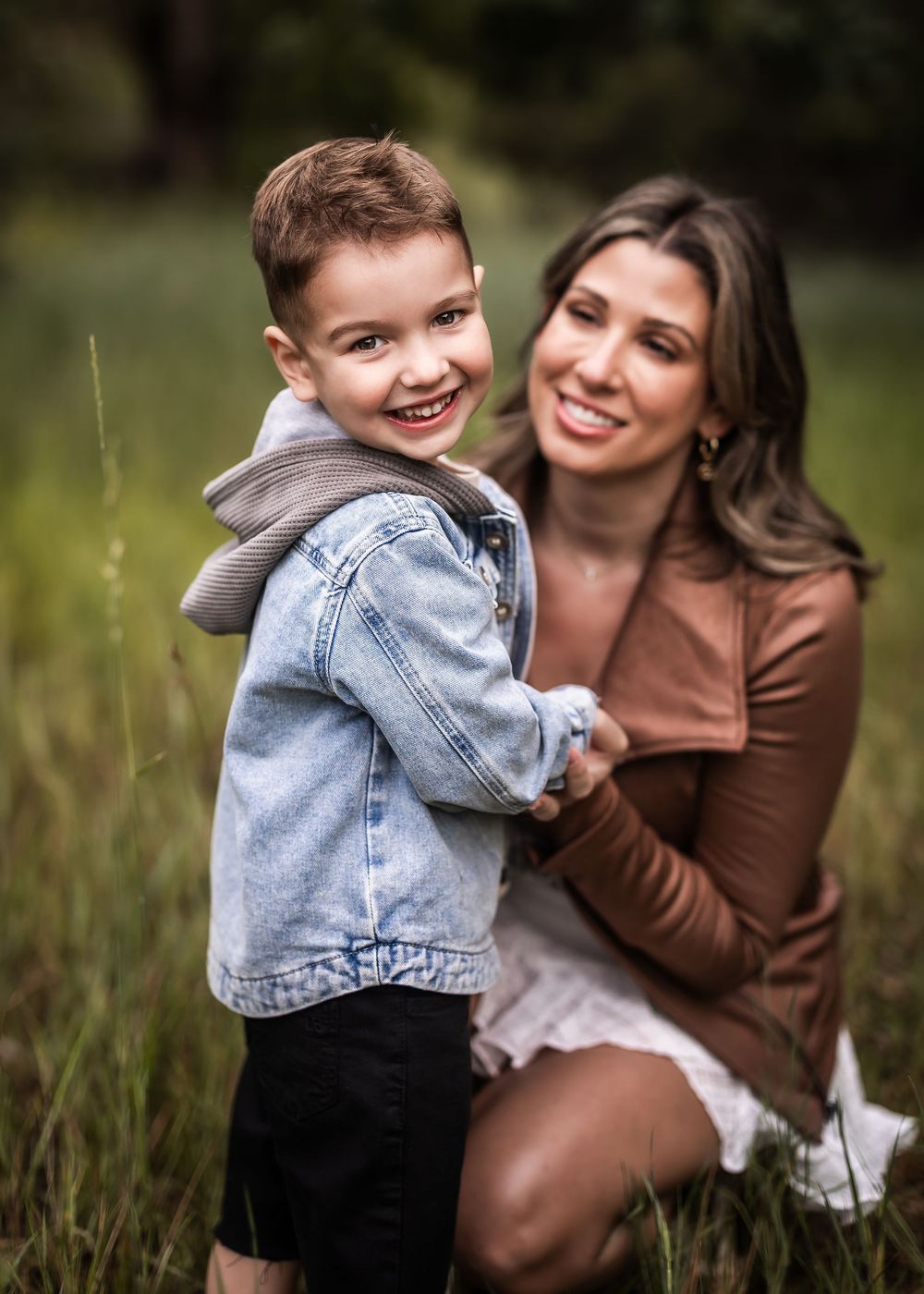 Mother and young child share joyful moments together in casual outfits while playing outdoors in tall grass.
