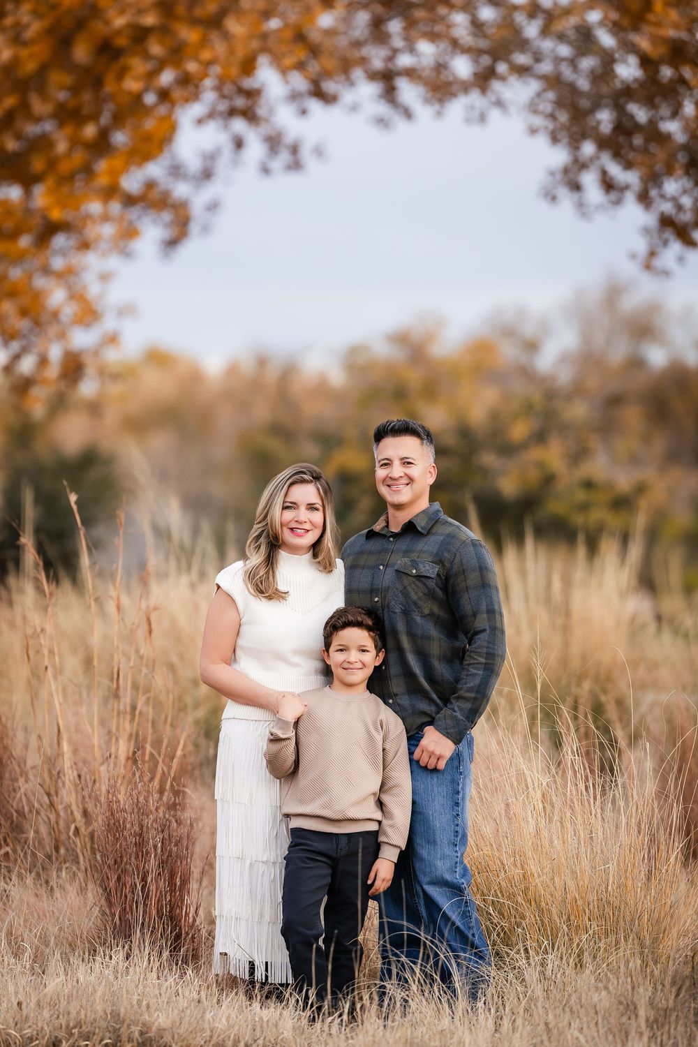 A family poses together in a field of tall golden grass during autumn with trees in the background.