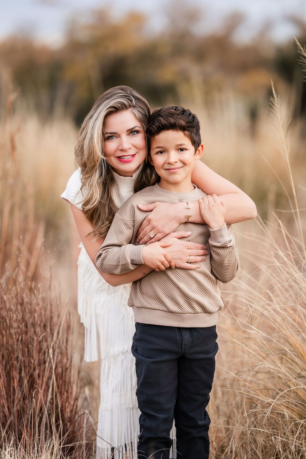 A tender embrace captured in a field of tall grass during golden hour with soft natural lighting.