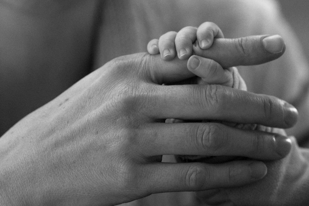 Mains parentales tenant celle d'un bébé, photo de naissance intime et poétique à Beersel, Rhode-Saint-Genèse, Bruxelles et alentours