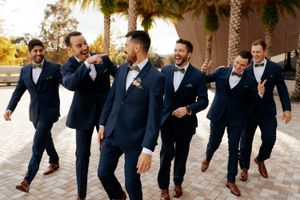 A playful groomsmen photo series showing men in navy suits jumping and posing together outdoors.