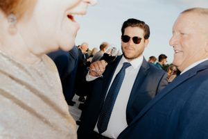 Wedding party members in formal attire chat and laugh together during an outdoor celebration.