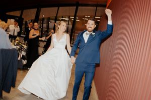 A couple celebrates during their wedding reception, with the bride in white and the groom in a navy blue suit.