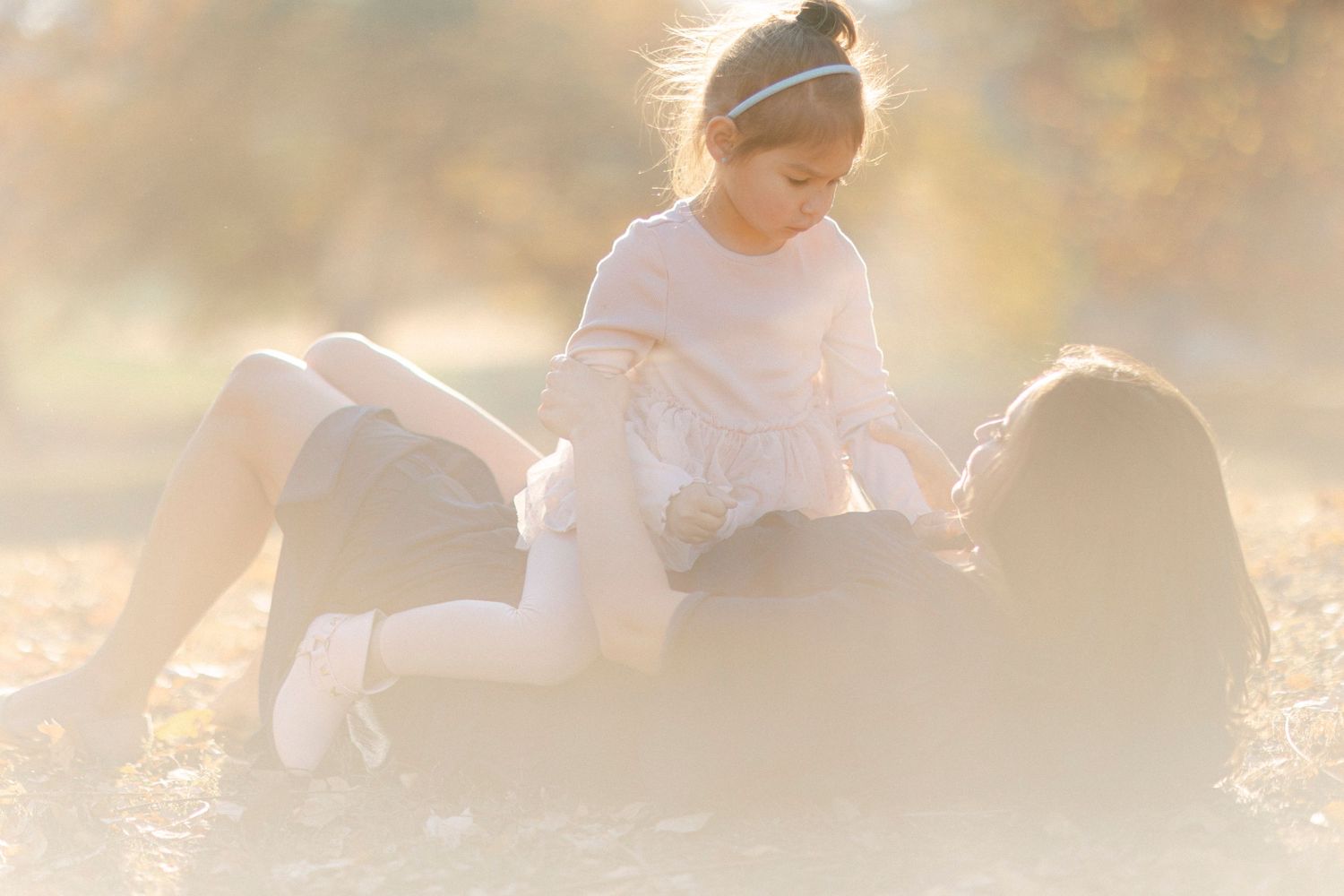 A playful moment captured in golden sunlight between two figures lying in grass.