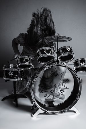 Dynamic black and white photo of long-haired drummer in action playing decorated drum kit with star motifs.