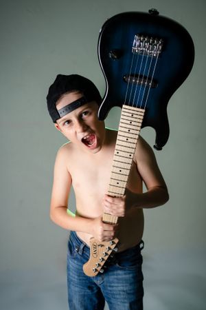 Young energetic musician strikes a pose with a blue electric guitar against a gray backdrop.