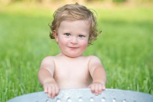 A young toddler with curly hair smiling while sitting outdoors in green grass.