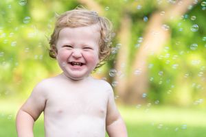 Joyful toddler laughs outdoors in a sunny garden with floating bubbles and green nature background.