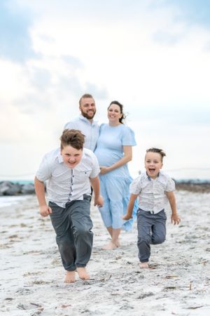 A joyful family runs and plays together barefoot on a sandy beach at sunset.