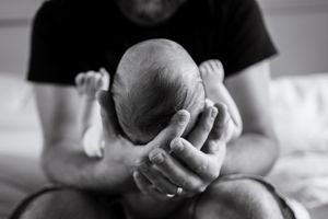 Black and white photo of hands cradling a newborn baby against a light background.