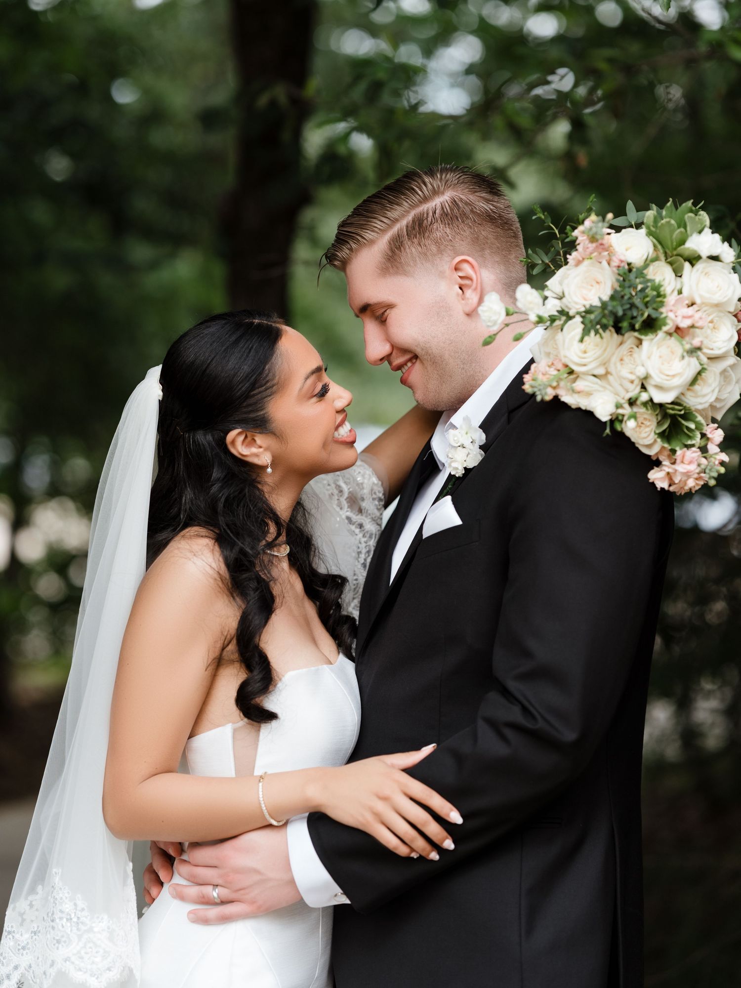 A wedding couple poses under a floral arch near a lake with the groom leading his bride by hand.