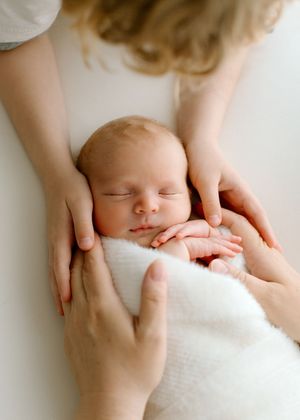 A sleeping newborn swaddled in white blanket being gently cradled by caring hands.