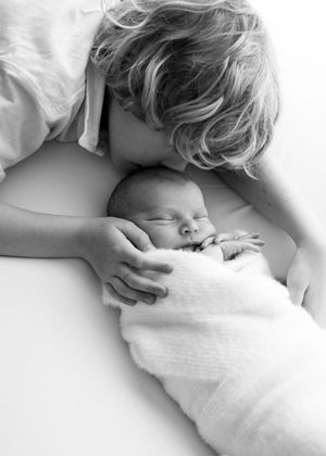A tender black and white photo of loving parent snuggling close to sleeping newborn baby wrapped in soft blanket.