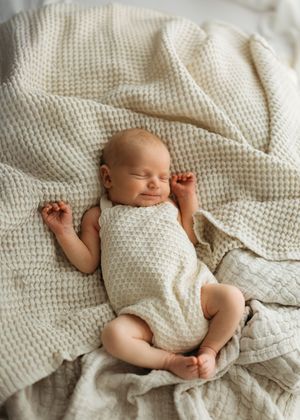 A peaceful sleeping newborn baby lying on textured white waffle knit blankets with arms outstretched.