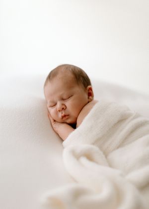 A peaceful newborn baby sleeps soundly while swaddled in soft white blankets.