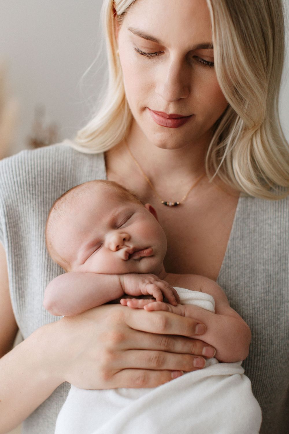 Tender moment of parent cradling sleeping newborn against soft gray sweater.